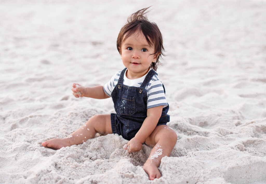 Baby boy wearing blue denim overall playing the sandy beach of Johnson Beach Perdido Key Florida