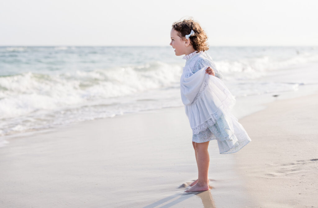 little girl wearing a blue flowery beautiful dress playing the salty water of Perdido Key Beach Florida